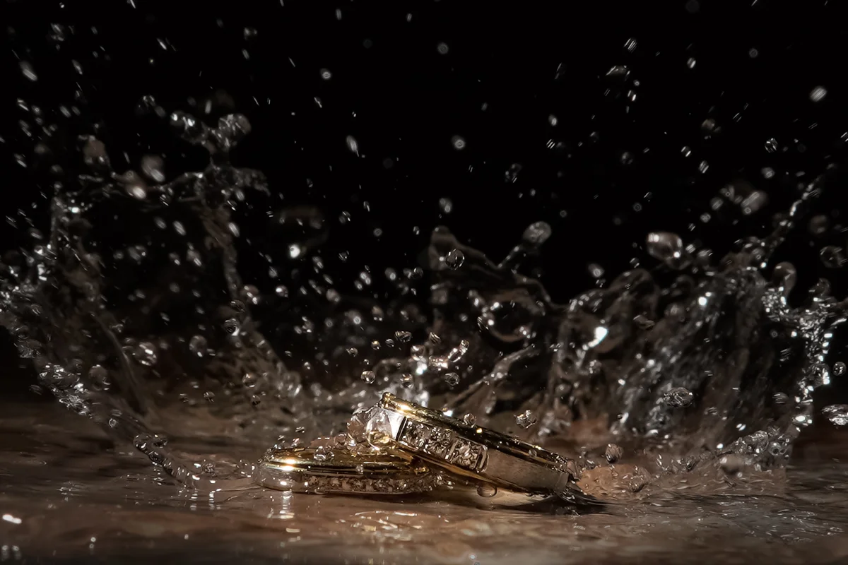 Wedding rings resting in a splash of water, lit against a dark background